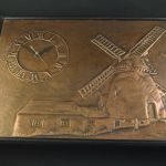 Ingelijst koperrelief (van een molen) met wandklok
